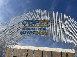 Der Eingang zur COP27 in Sharm-El-Sheikh 2022. Ein Bogen aus Metallstäben und der Aufschrift in Blau und Gold: "COP27 Sharm El-Sheikh Egypt 2022".