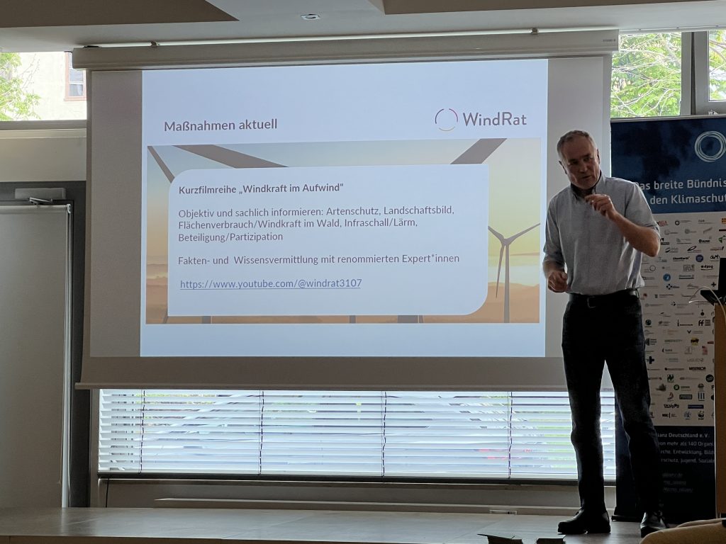 Peter Keller präsentiert auf dem Plenum der Klima-Allianz Duetschland den WindRat. Er steht vor einer Vortragsfolie zur Kurzfilmreihe "Windkraft im Aufwind"