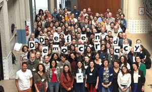 Man sieht Menschen die auf Schildern den Schriftzug Defend Democracy hochhalten