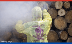 Ein Mensch in gelbem Schutzanzug vor wuchtigen Holzbaumstämmen. Er trägt Atemschutzmasken und ein Gas wabert um ihn herum, das das Pestizid ProFume symbolisiert.